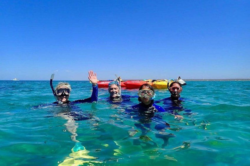 People snorkeling in clear blue water with a boat in the background. 2