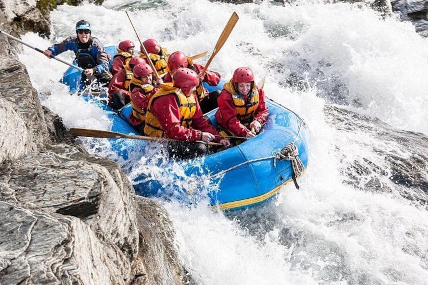 Un groupe de personnes à bord d’un radeau bleu naviguant dans des rapides aux eaux tumultueuses. 3