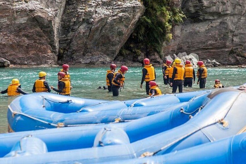 Des personnes portant des gilets de sauvetage jaunes et des casques rouges se trouvent près de bateaux pneumatiques bleus sur une plage rocheuse. 2