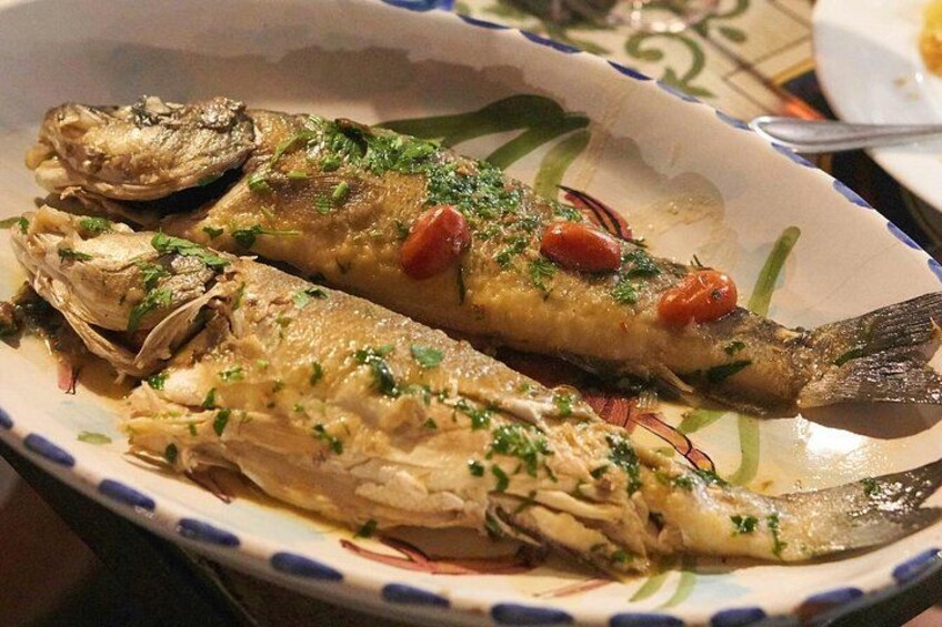 A plate of cooked fish garnished with herbs and tomatoes. 4