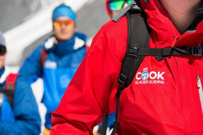 Una persona con chaqueta roja con el texto 'MT Cook Glacier Guiding'. 2