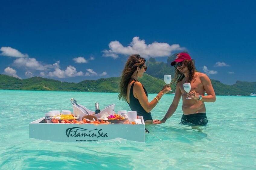 Two people on a boat in clear turquoise water with a tropical landscape in the background. 2