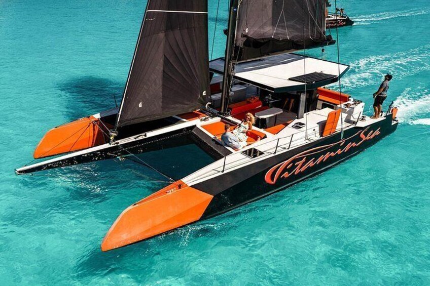 A catamaran with two large orange hulls and a black superstructure sailing on turquoise water. 3