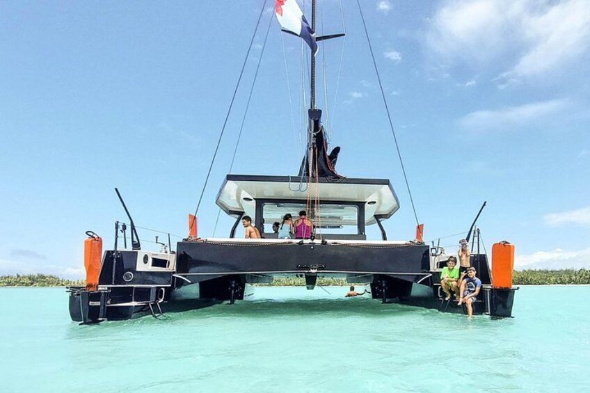 A sailboat on turquoise water with a flag, people on deck, and a clear sky. 3