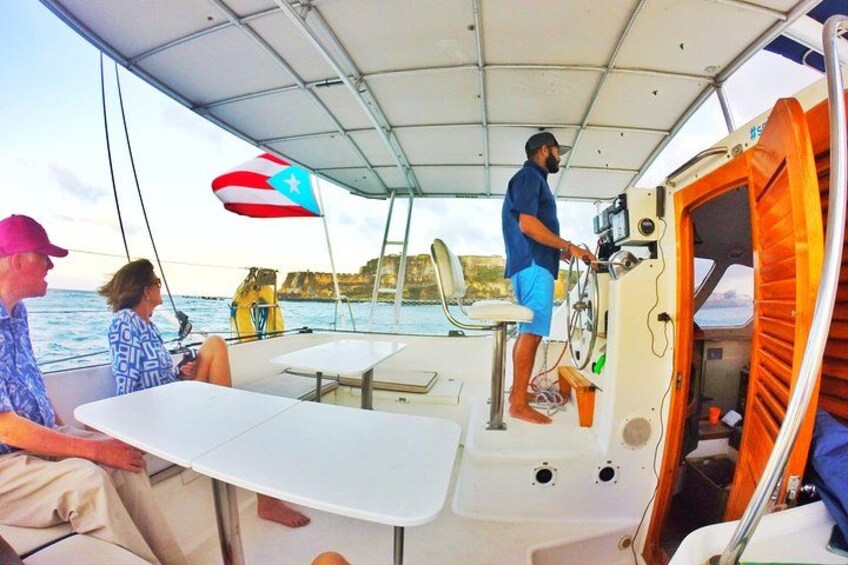 A sailboat with a person standing at the helm, a table, and a flag. 2