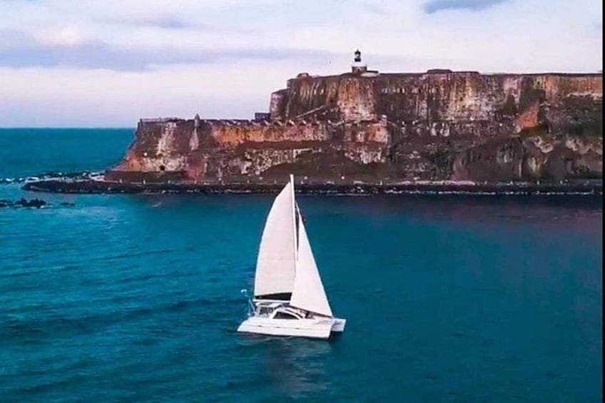 A sailboat on calm blue waters with a rocky cliff and lighthouse in the background. 3