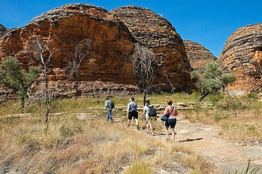 A group of hikers on a rocky trail with red sandstone formations in the background. 1