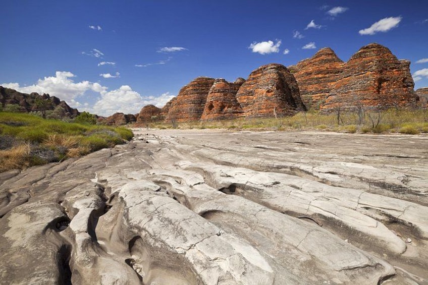 A rocky landscape with layered sedimentary rock formations and sparse vegetation under a clear blue sky. 2