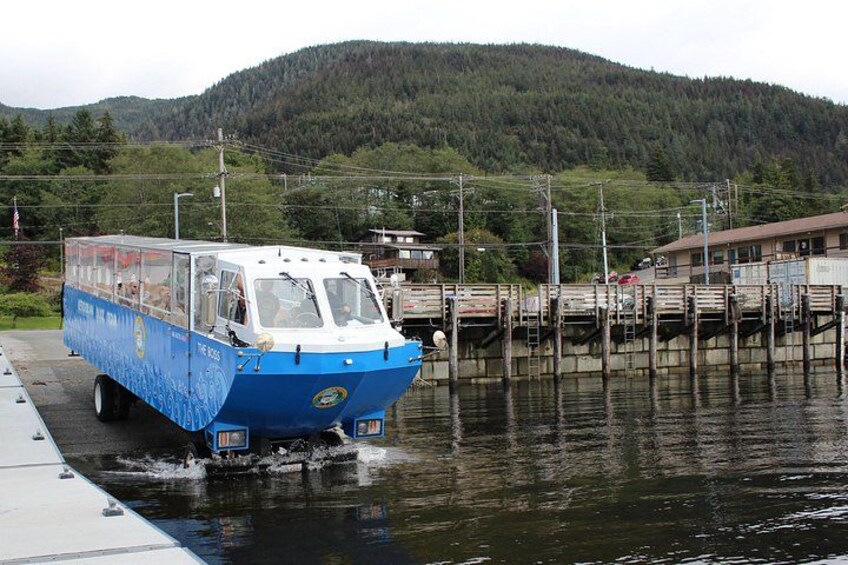 En blå og hvid båd ligger til kaj ved en bro, med et skovdækket bjerg i baggrunden. 1