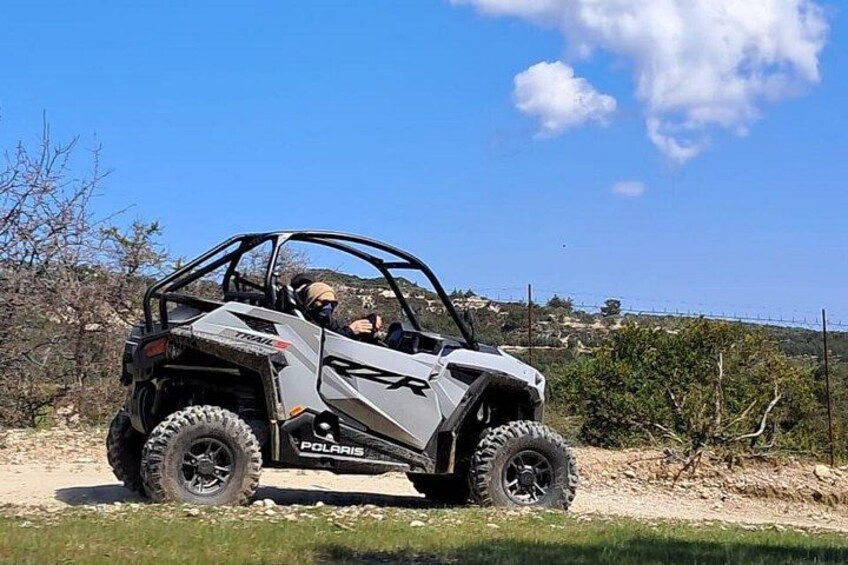 En Polaris fyrhjuling på en grusväg med ett kuperat landskap i bakgrunden. 1