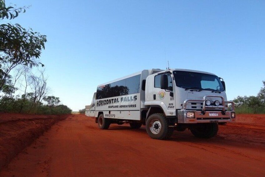 A white truck with 'HORIZONTAL FALLS' and 'SEA PLANE ADVENTURES' on the side, parked on a red dirt road with sparse vegetation. 2