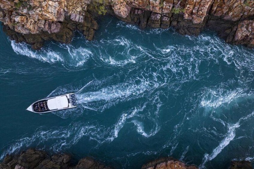 A boat navigating through a turbulent sea with rocky cliffs in the background. 1