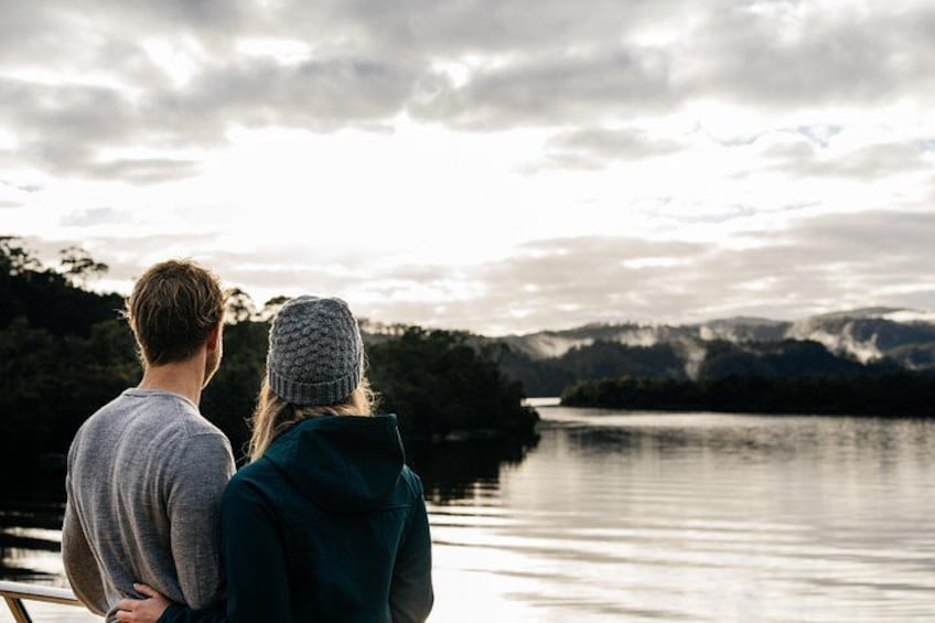 Deux personnes se tiennent près d’un lac, avec des montagnes en arrière-plan. 1