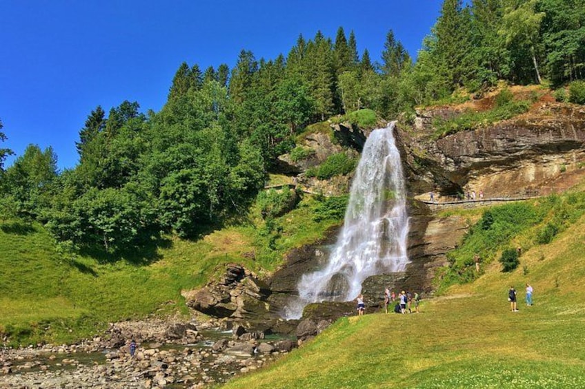 Een waterval stort neer over een rotswand, omringd door weelderige begroeiing. 1