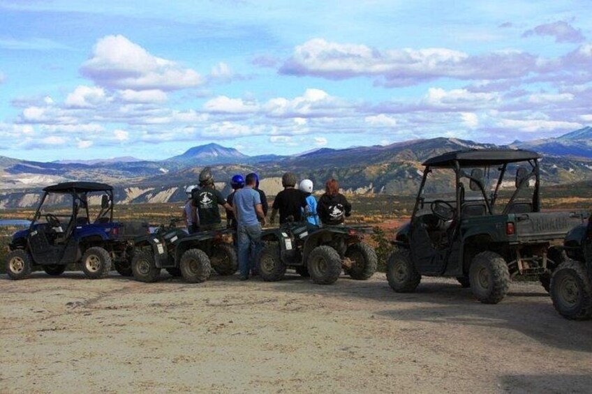 A group of people on all-terrain vehicles (ATVs) in a barren landscape with mountains in the background. 3