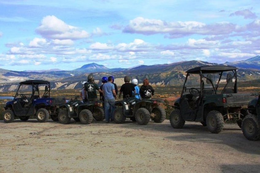 A group of people on all-terrain vehicles (ATVs) in a desert landscape with mountains in the background. 3
