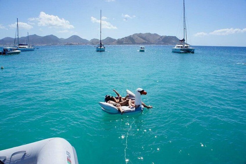 A turquoise sea with boats and a person on a raft. 5
