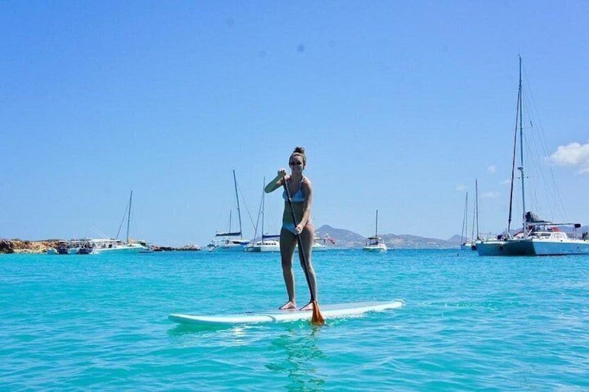 A person surfing on a clear blue sea with boats in the background. 2