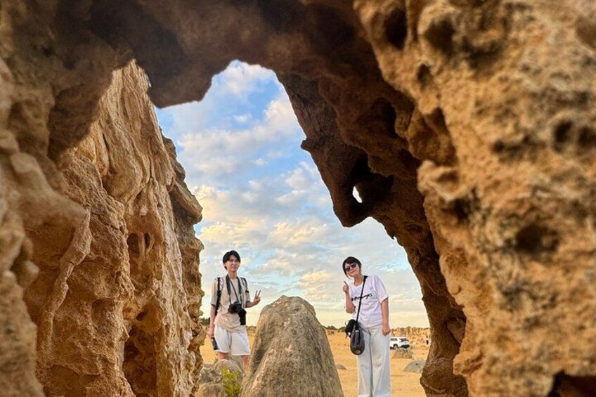 Dos personas de pie en una cueva rocosa, con un cielo despejado al fondo. 3