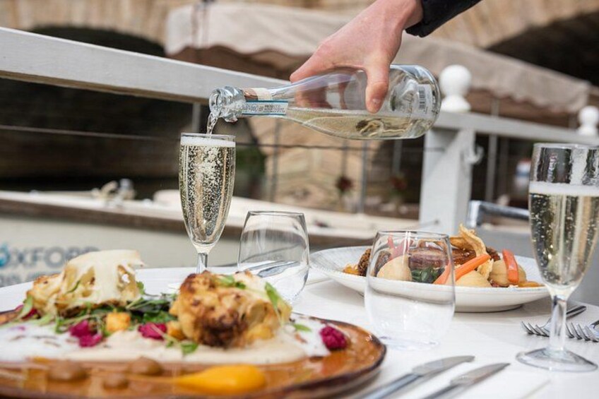 Iemand schenkt een drankje in een glas, een bord eten en nog een glas staan op tafel. 1