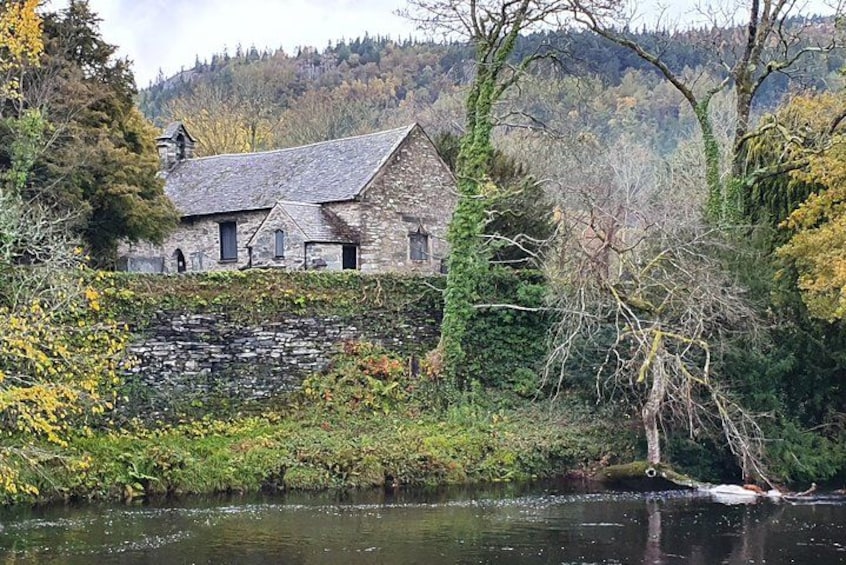 A stone house by a river with a stone wall and trees in the background. 4