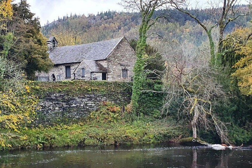 A stone house by a river, surrounded by trees and a stone wall. 4