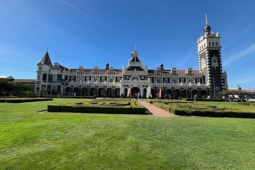 Un edificio grande e histórico con una torre de reloj, rodeado de céspedes cuidados y un cielo azul despejado. 1
