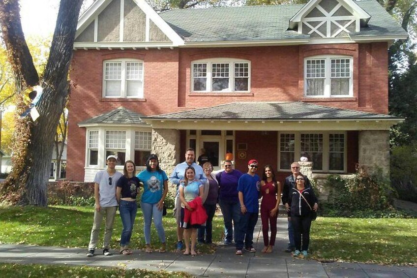 A group of people standing in front of a brick house with a porch. 5