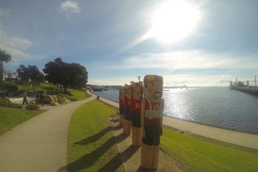 A pathway beside a body of water, with a sculpture of a character in a red shirt and black shorts. 2