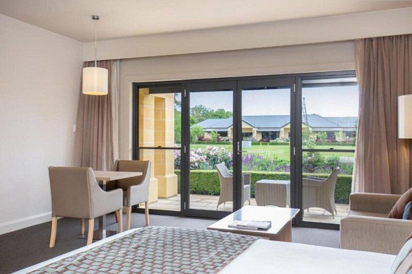 A hotel room with a bed, a desk, a chair, and a view of a garden through a sliding glass door. 3