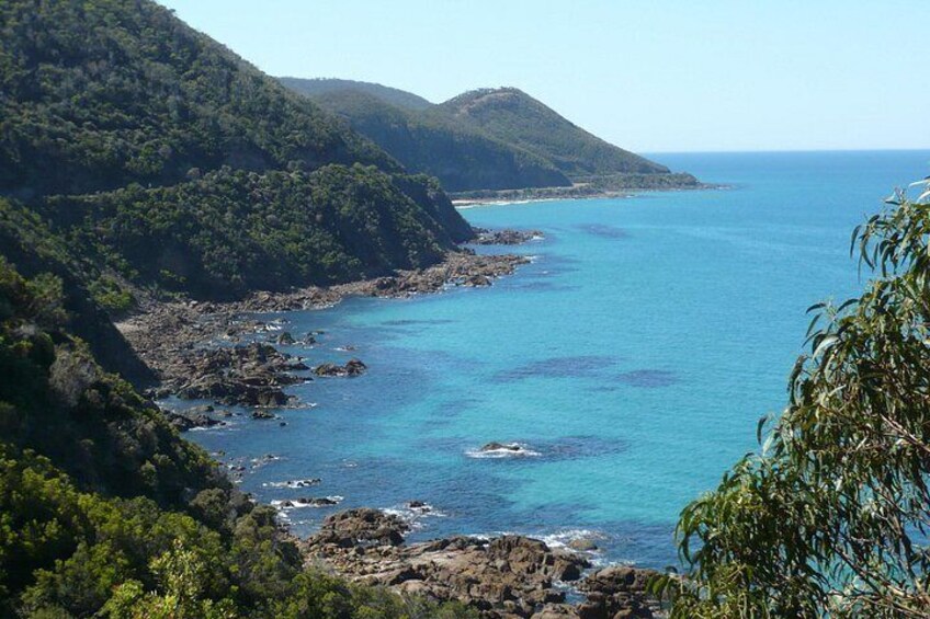 A coastal landscape with clear blue waters, rocky shores, and lush green hills. 3
