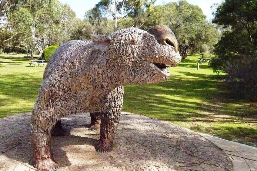 A dinosaur statue in a park with trees and a picnic area in the background. 2