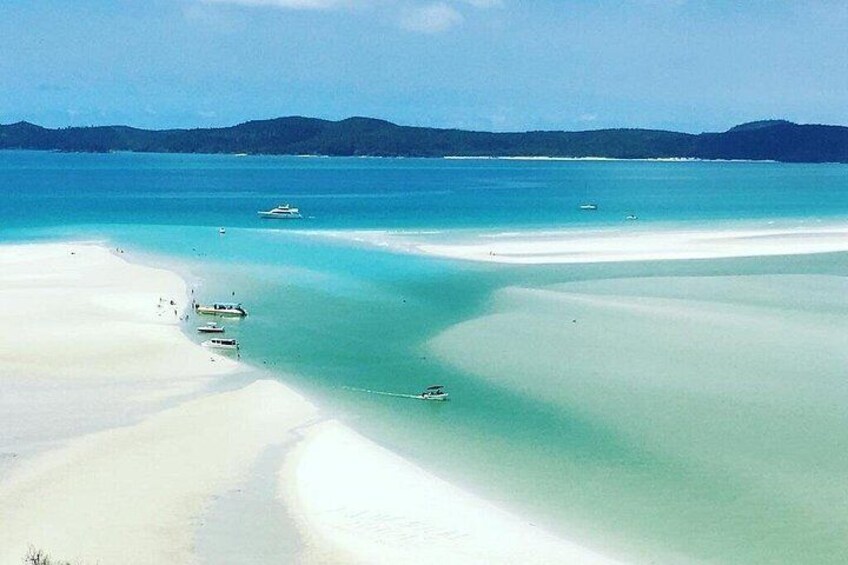A beach with clear turquoise waters, white sand, and boats. 1