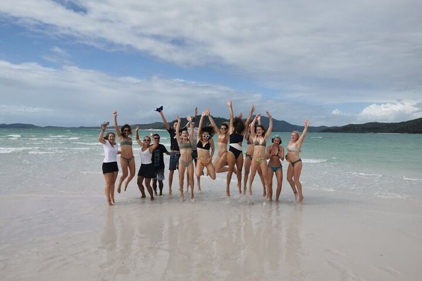 Un gruppo di persone salta su una spiaggia sotto un cielo sereno e un mare calmo. 5