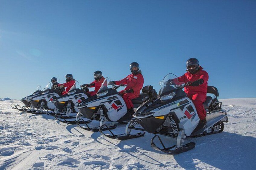 Three people in red snowmobiles on a snowy landscape. 4