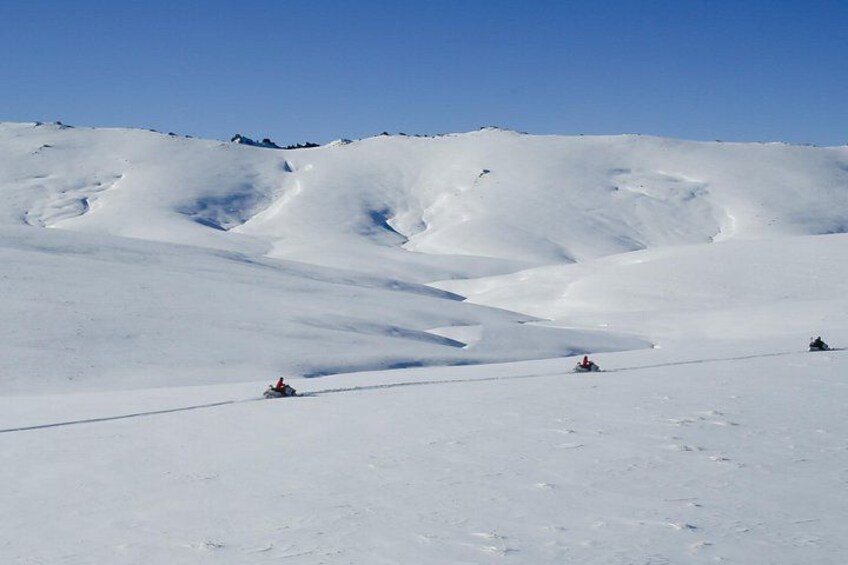 A snowy mountain landscape with three skiers on a slope. 3
