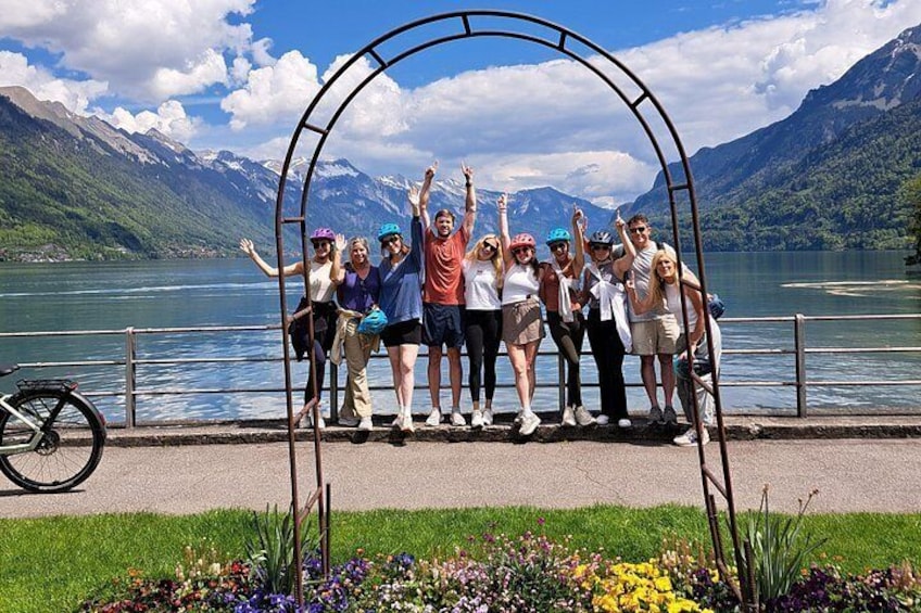 A group of people posing in an archway by a lake with mountains in the background. 5