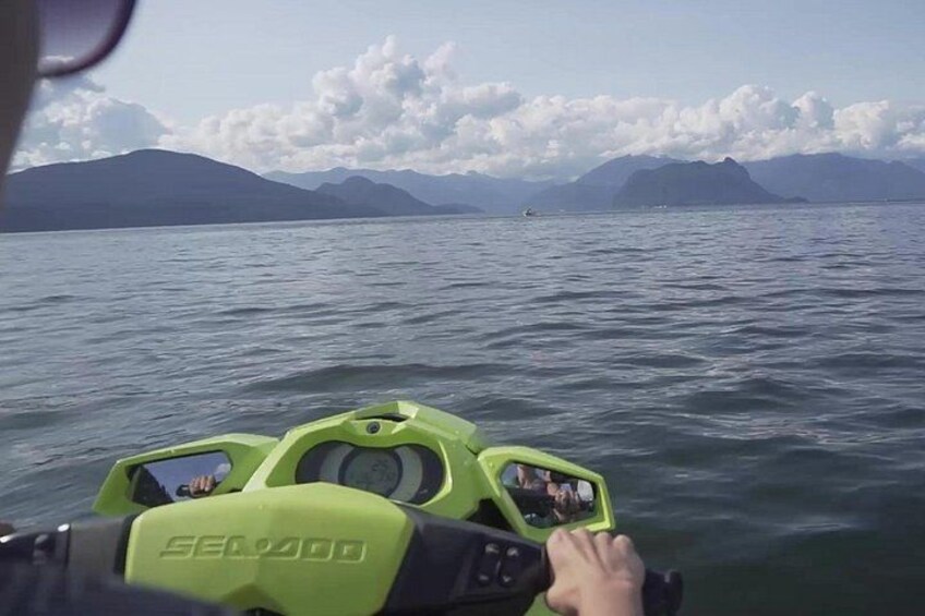 A person steering a green Sea-Doo jet ski on a body of water with mountains in the background. 5