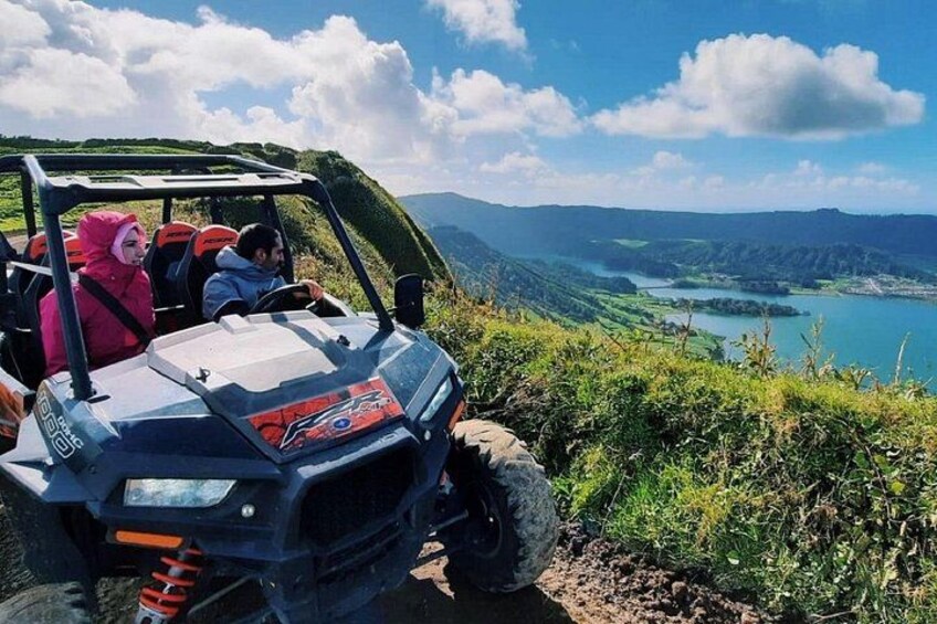 A vehicle on a mountain road with a lake in the background. 1