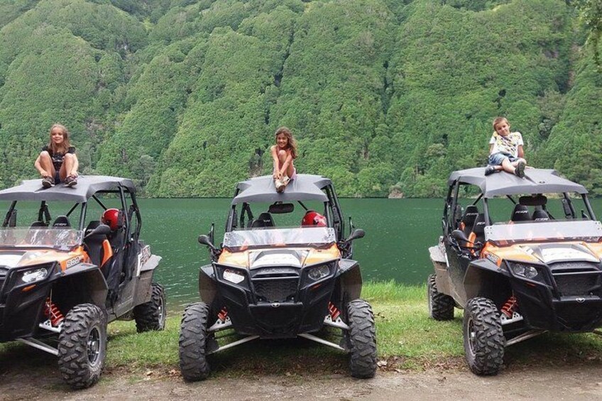 Three all-terrain vehicles parked by a lake with people on them. 4