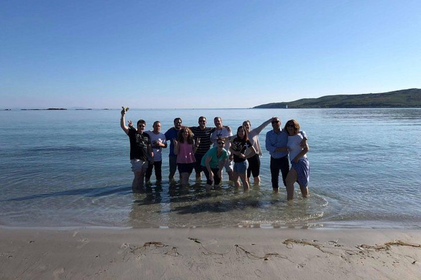Un groupe de personnes se tient dans une eau peu profonde sur une plage, avec un ciel dégagé et une terre lointaine en arrière-plan. 3