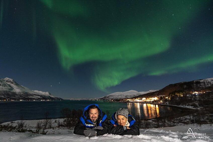 A snowy landscape with a lake, a person wearing a blue jacket, and the Northern Lights in the sky. 2