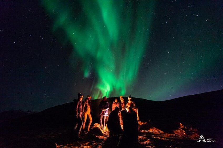 A group of people standing on a hill under a night sky with green aurora borealis. 1