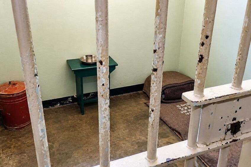 A jail cell with a green table, a red bucket, and a brown bag. 5