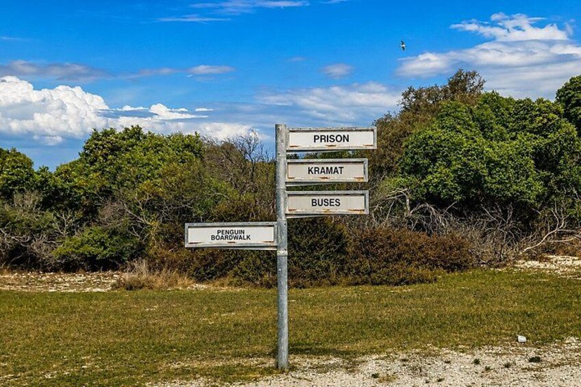 A directional signpost with multiple signs pointing to 'Prison', 'Kramat', 'Buses', and 'Penguin Boardwalk'. 5