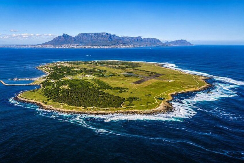 An aerial view of a green island surrounded by blue ocean waves, with a mountain range in the background. 1