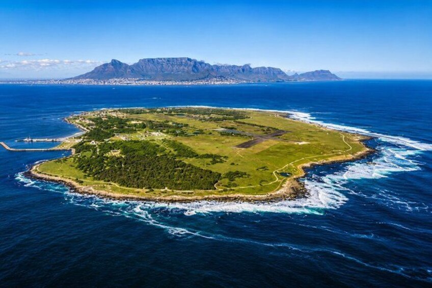 An aerial view of a green island surrounded by blue ocean waves, with a mountain range in the background. 1