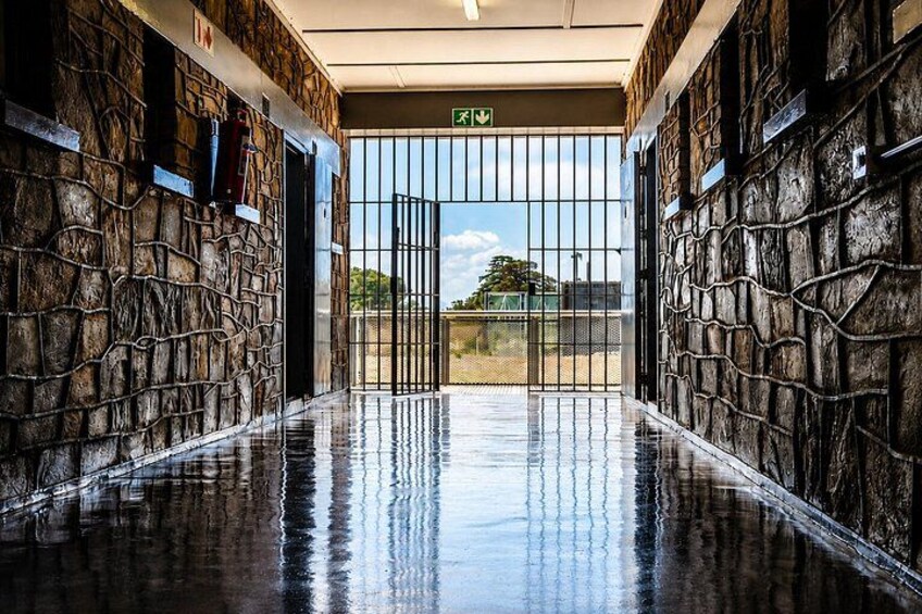 A wet stone corridor with a metal gate and an exit sign. 4