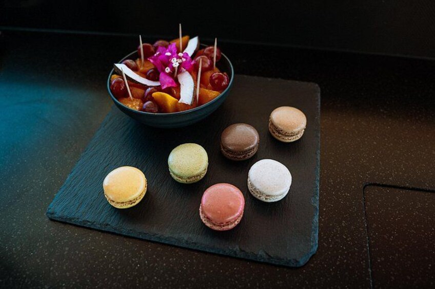 A bowl of fruit and macarons on a slate board. 4