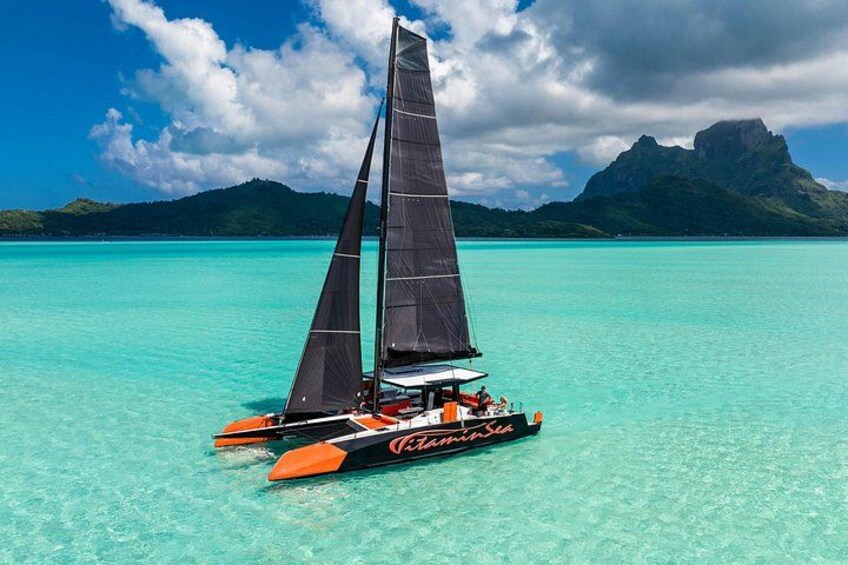 A sailboat named 'Camarina Sea' on turquoise waters with mountains in the background. 1
